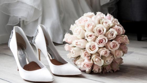 A pair of white wedding heels and a light pink wedding bouquet beside it