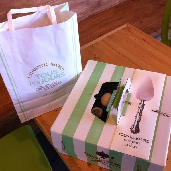 A box of Tous Les Jours on the wooden table and its paper bag beside it